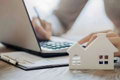 Foto: Person bearbeitet Akten, Modell eines Hauses im Vordergrund